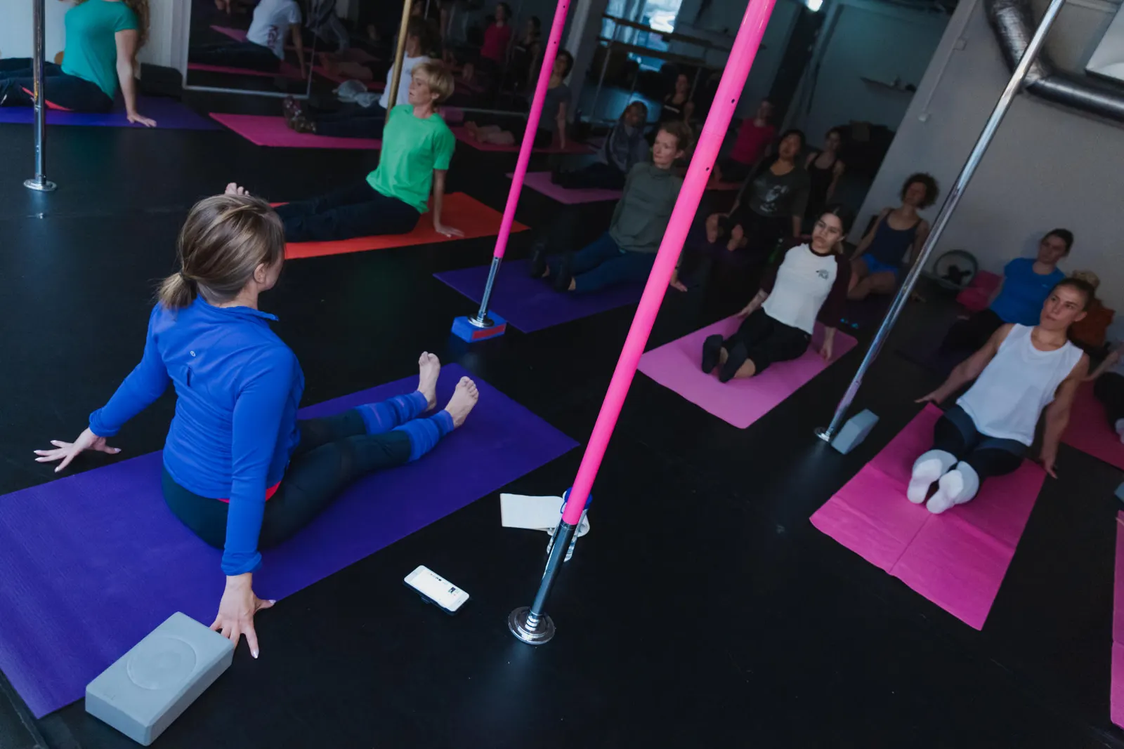 Students stretching between pink poles in the pole studio