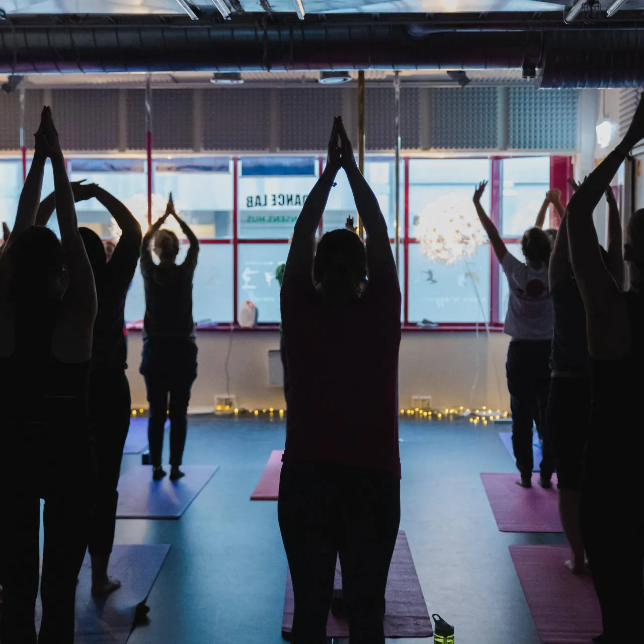 A yoga class with raised arms in front of large windows